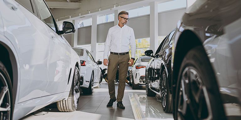 Homem entre carros está em dúvida sobre a melhor opção: Leasing, ALD, Renting ou Crédito Automóvel