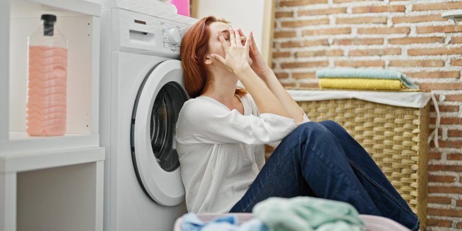 Mulher com as mãos no rosto encostada à máquina de lavar porque não sabe como lidar com despesas inesperadas