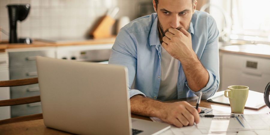 Homem olha para o computador preocupado porque está com dificuldade em pagar as contas