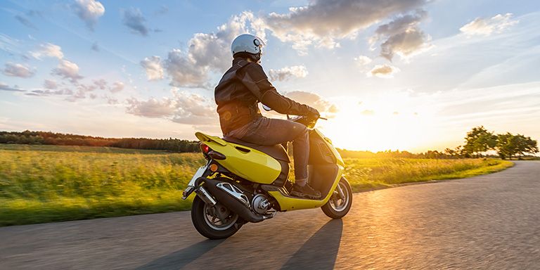 Scooter amarela em estrada junto a campo. Um sonho? Saiba como financiar a compra de uma mota.