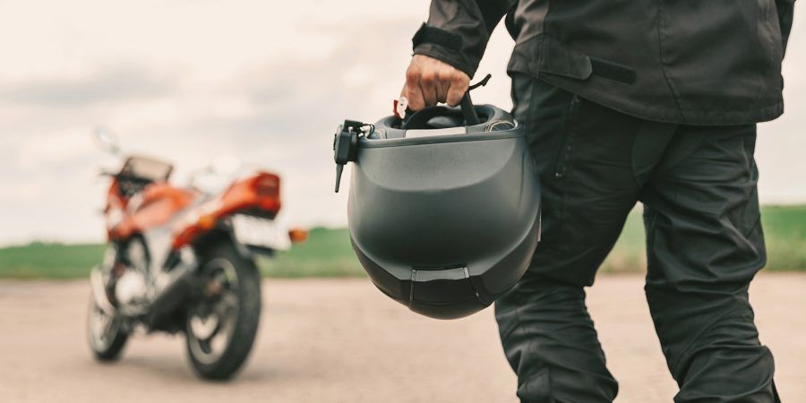 Motociclista com capacete na mão e moto ao fundo pergunta-se "será a inspeção de motos obrigatória?"
